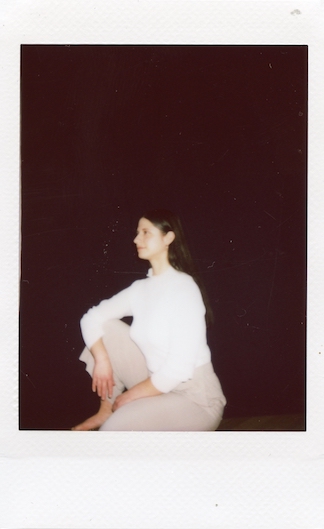 seitliche Ansicht von Geburtsbegleiterin Maria-Lisa sitzt auf dem Boden, ein Fuß aufgestellt, sie sieht zu einem Punkt, den man im Bild nicht sieht , als würde sie jemanden ansehen